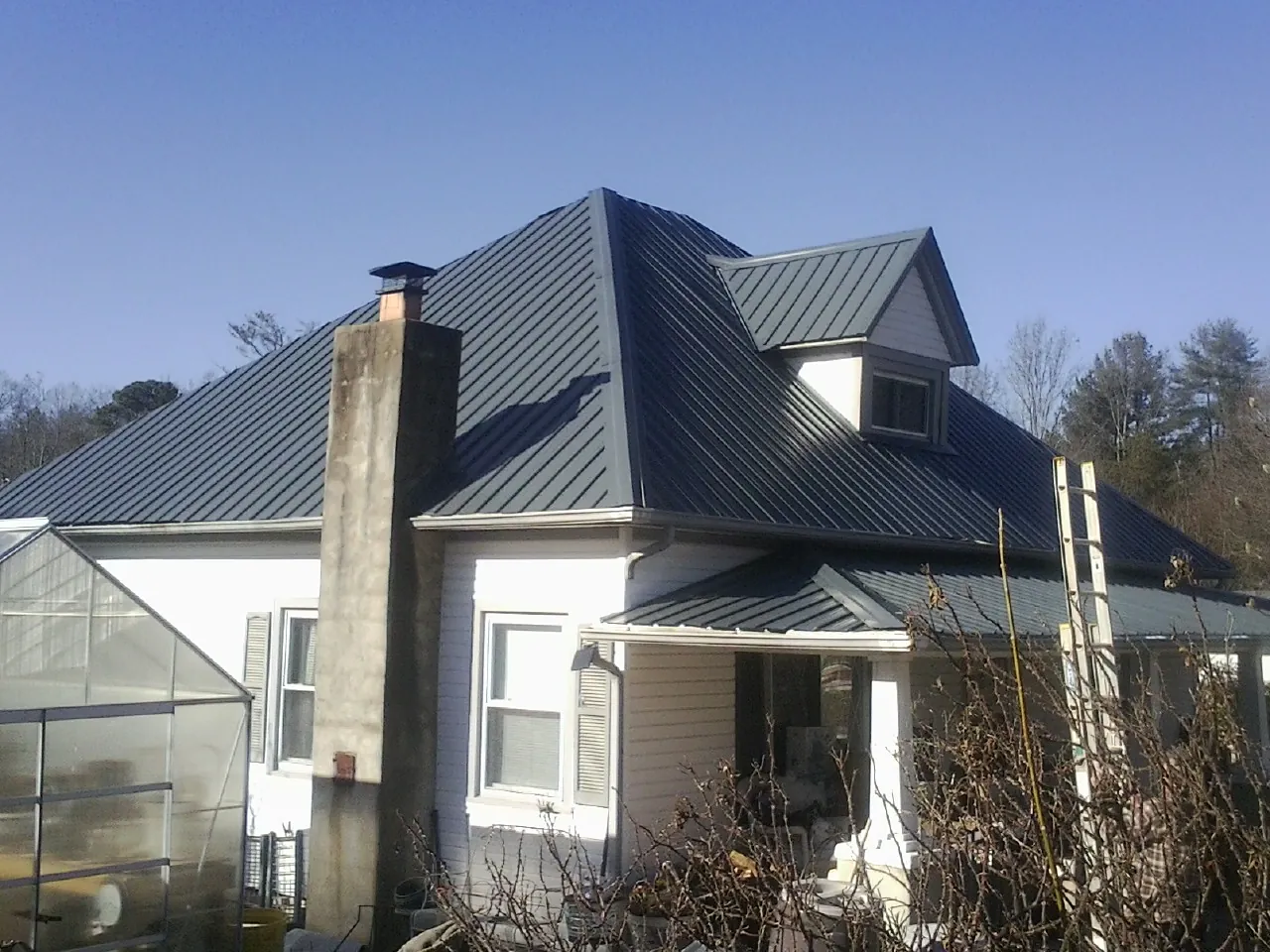 Dark blue standing seam metal roof on a white farmhouse with dormer — Slate & Tile Roof Repair by Roofing Brothers in Stamford