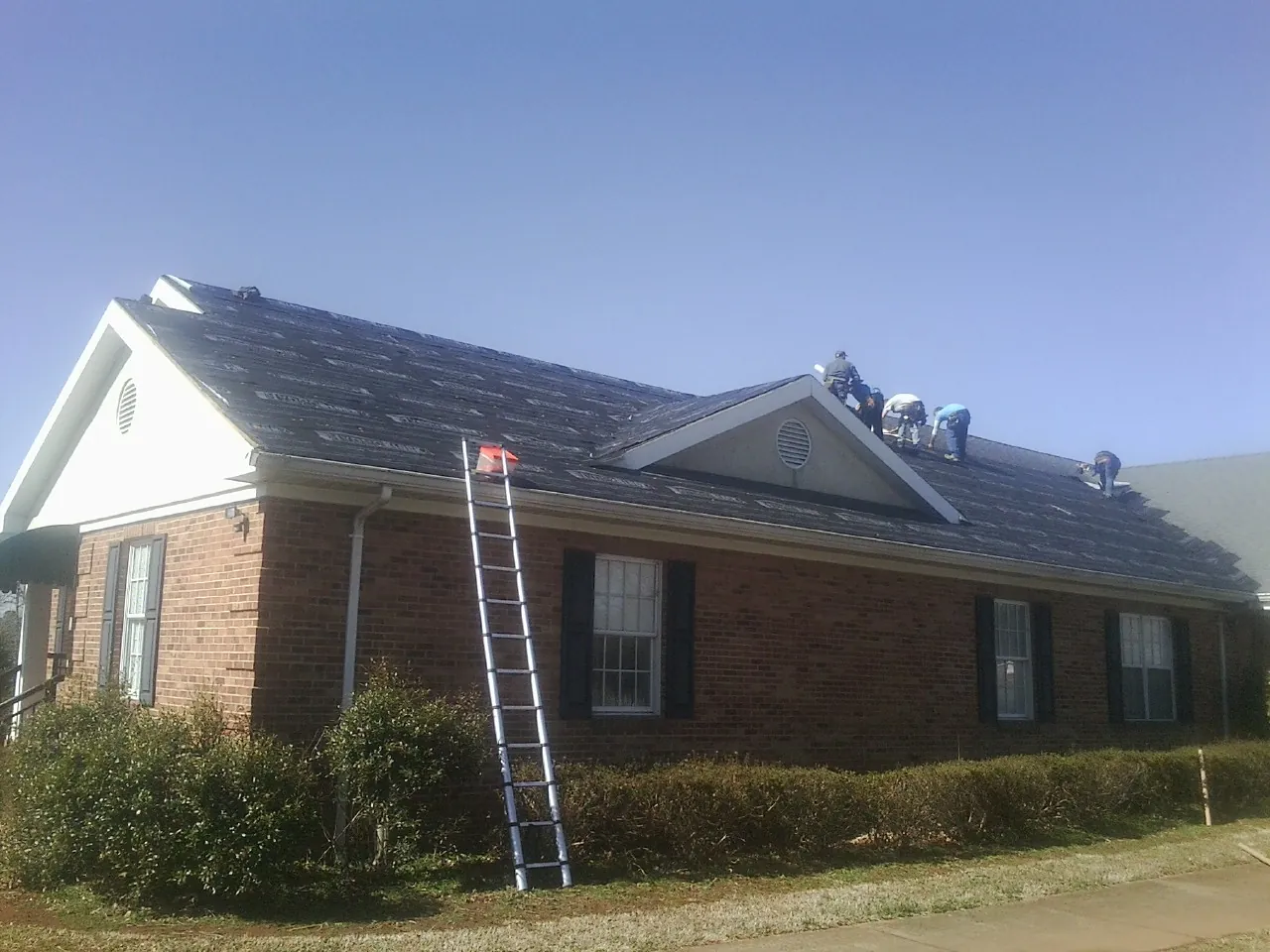 Crew tearing shingles off a brick ranch roof with a ladder set — Metal Roof Repair work by our crew in Stamford