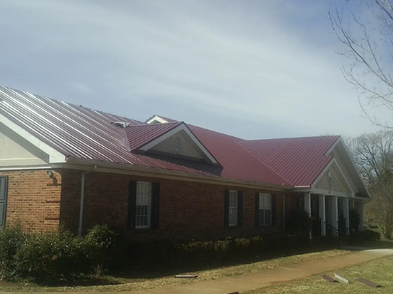 Red metal roof with gabled entries on a long brick building, from a Hail Damage Roof Repair job in Stamford