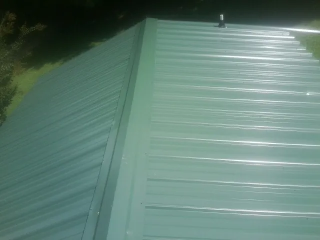 New green metal panels meeting at the ridge of a roof — Flat Roof Repair work by our crew in Stamford