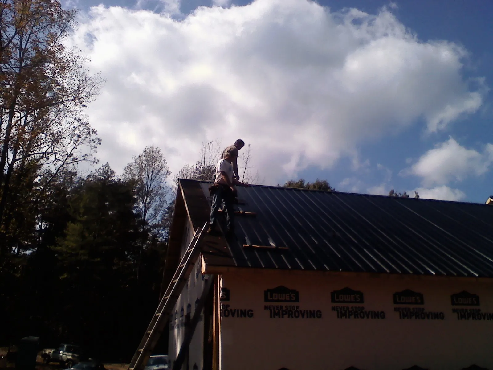 Roofer fastening dark metal panels high against a cloudy sky, from a Roof Inspection job in Stamford