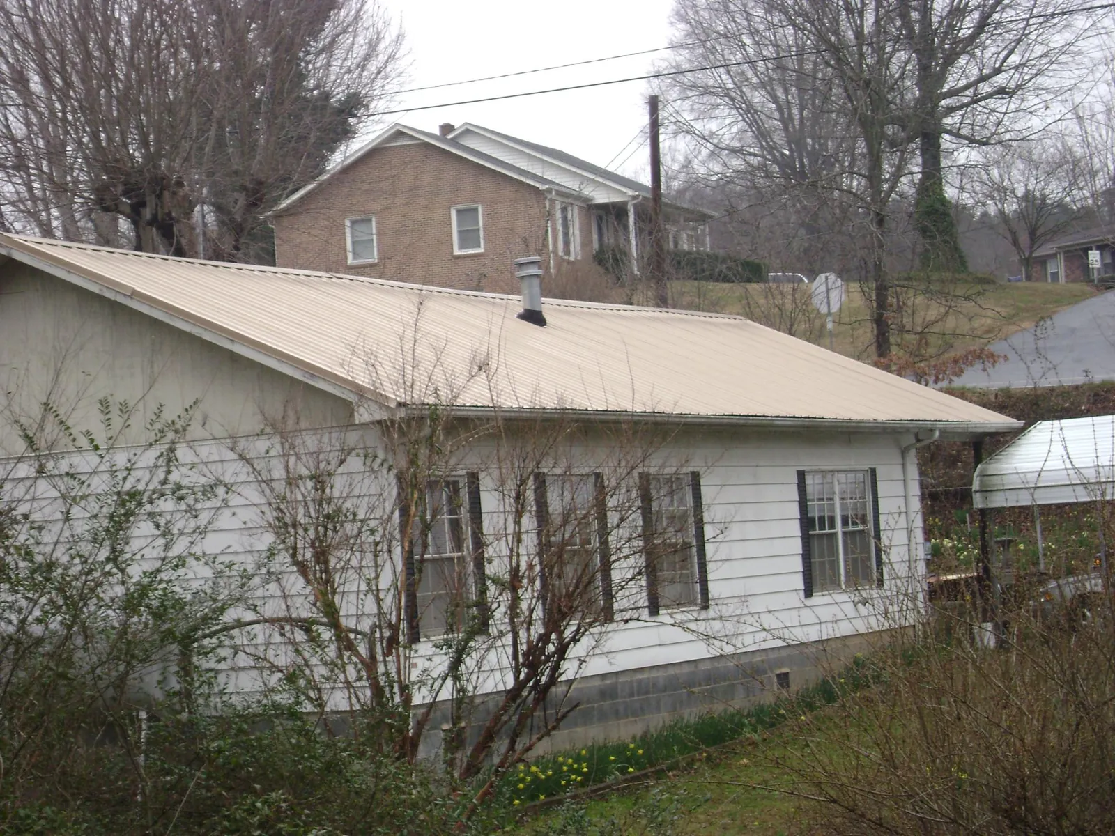 Tan metal roof on a white sided house set into a hillside — Commercial Roofing by Roofing Brothers in Stamford