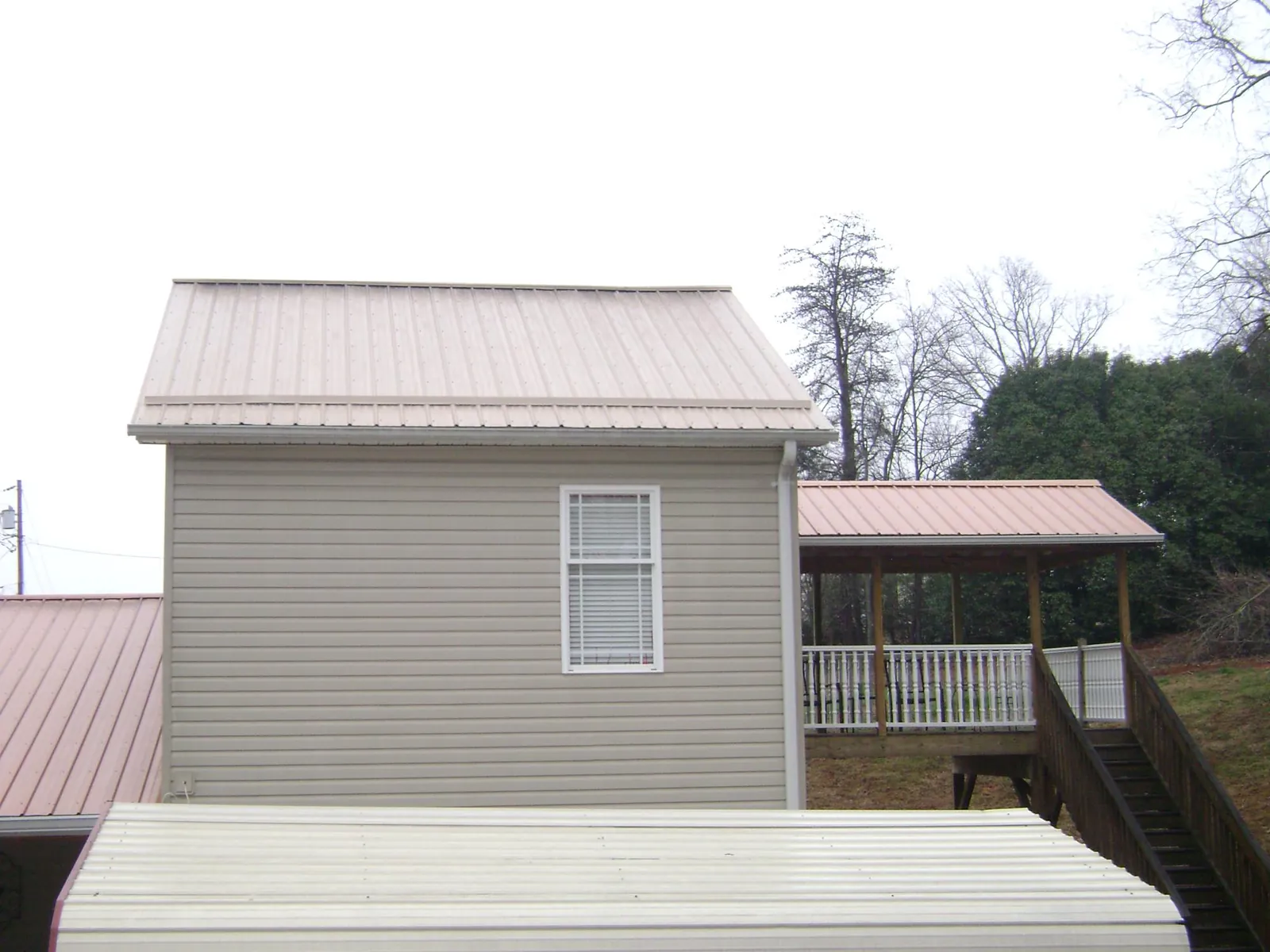 Tan metal roofs on a two story addition and attached porch, from a Roof Replacement job in Stamford